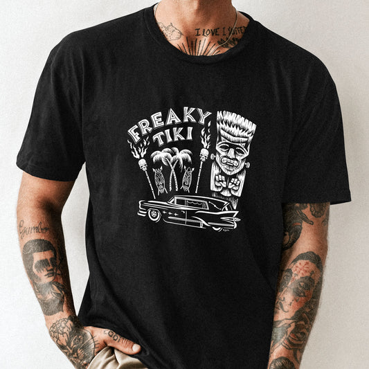 Black unisex tee shirt modelled by a man. Design is a white graphics with a vintage hearse, a frankenstein tiki and skull torches. The text says "Freaky Tiki"