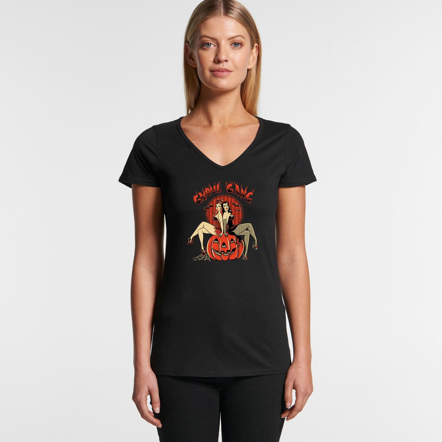 Ladies V-neck black Halloween T-shirt featuring two pinup witches sitting on a giant pumpkin. Text say "Ghoul Gang"