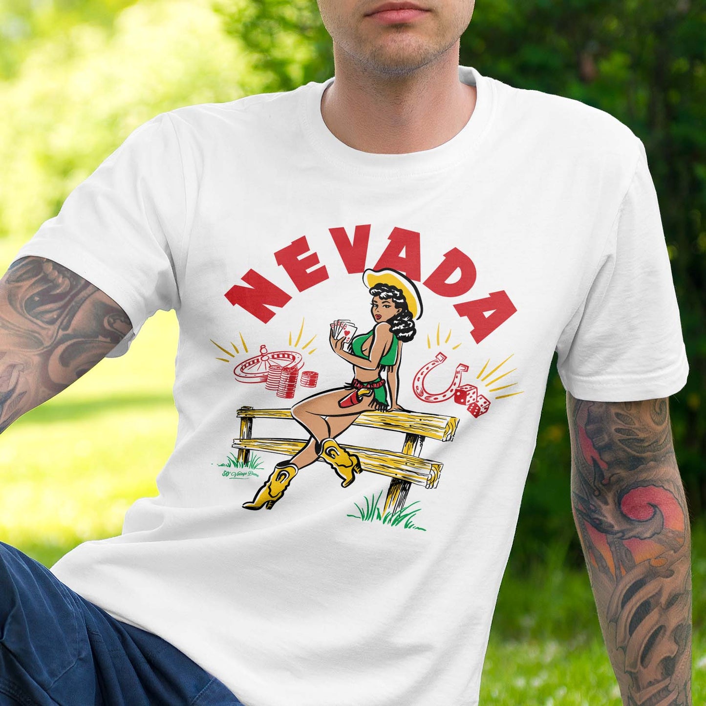 Vintage-style illustration by 50s Vintage Dame of a pinup cowgirl sitting on a wooden fence holding a Royal Flush. Headline says "Nevada" . WHite short-sleeved tee shirt.