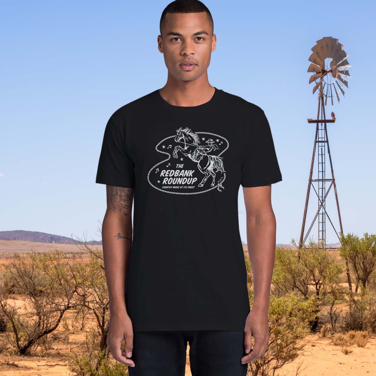 Black unisex t-shirt with a cowboy riding a bucking bronco. Text says "The Red Bank Roundup - country music at its finest" A lasso, stars and music notes surround the design.